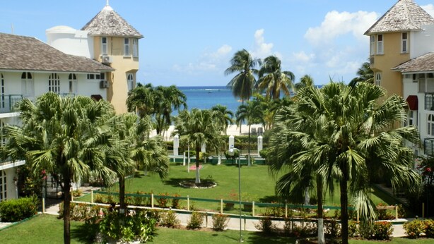 Un resort con varias construcciones, palmeras y vista a la playa.