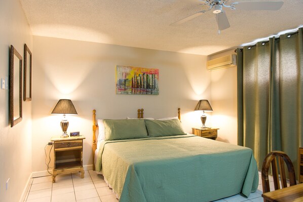 A neatly arranged bedroom with a bed, two bedside tables with lamps, a wall-mounted air conditioner, and a ceiling fan.