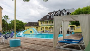 Un área de piscina con sillones de descanso, un tobogán y un edificio con varios balcones.