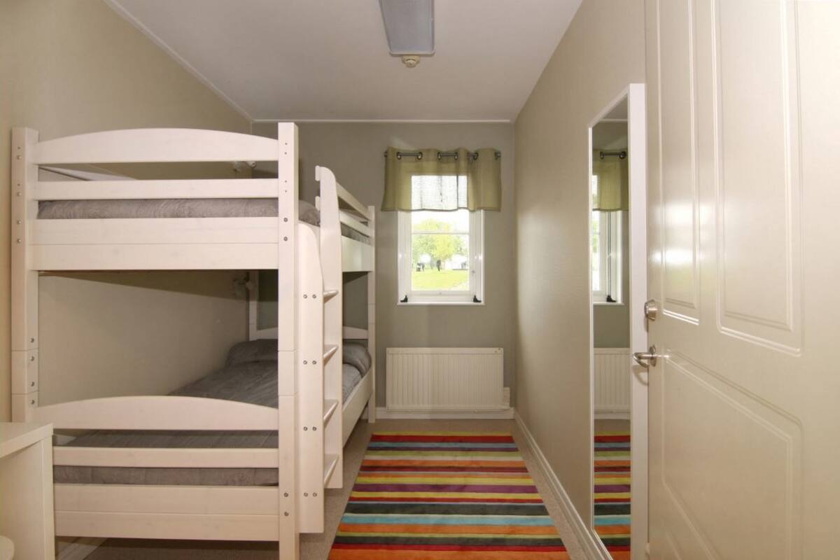 A bunk bed room with a window, a radiator, and a striped carpet.