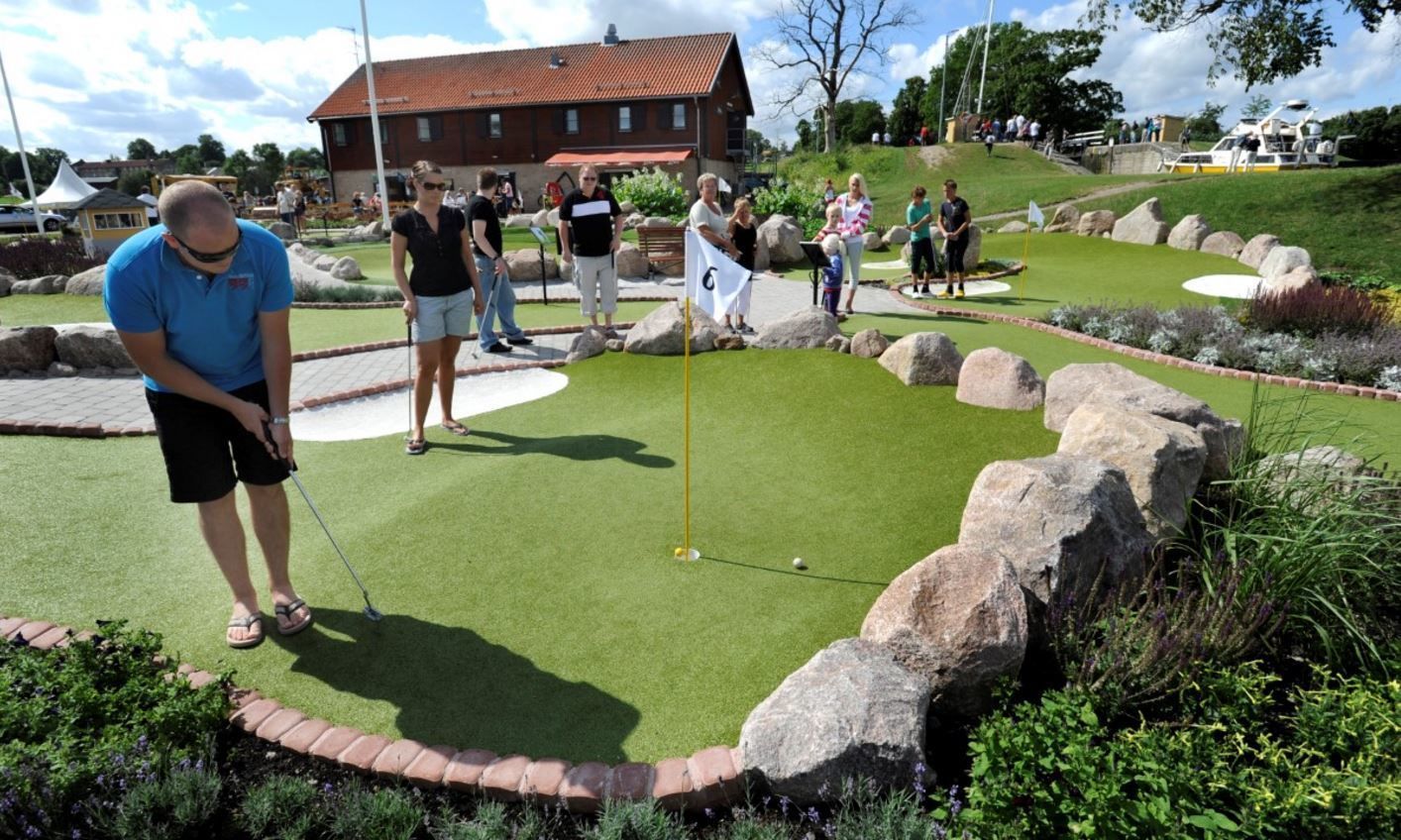 A miniature golf course with a putting green, a flag, and a brick border.