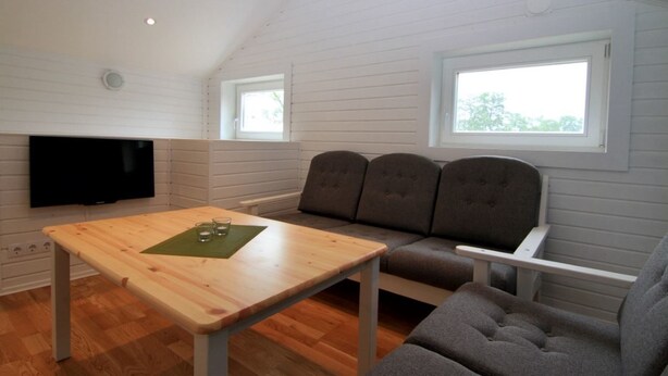 A room with a wooden table, grey upholstered sofa, and a flat-screen TV mounted on the wall.
