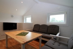 A room with a wooden table, grey upholstered sofa, and a flat-screen TV mounted on the wall. - Bergs Slussar Vandrarhem & Stugor - Hostel (Vreta Kloster)