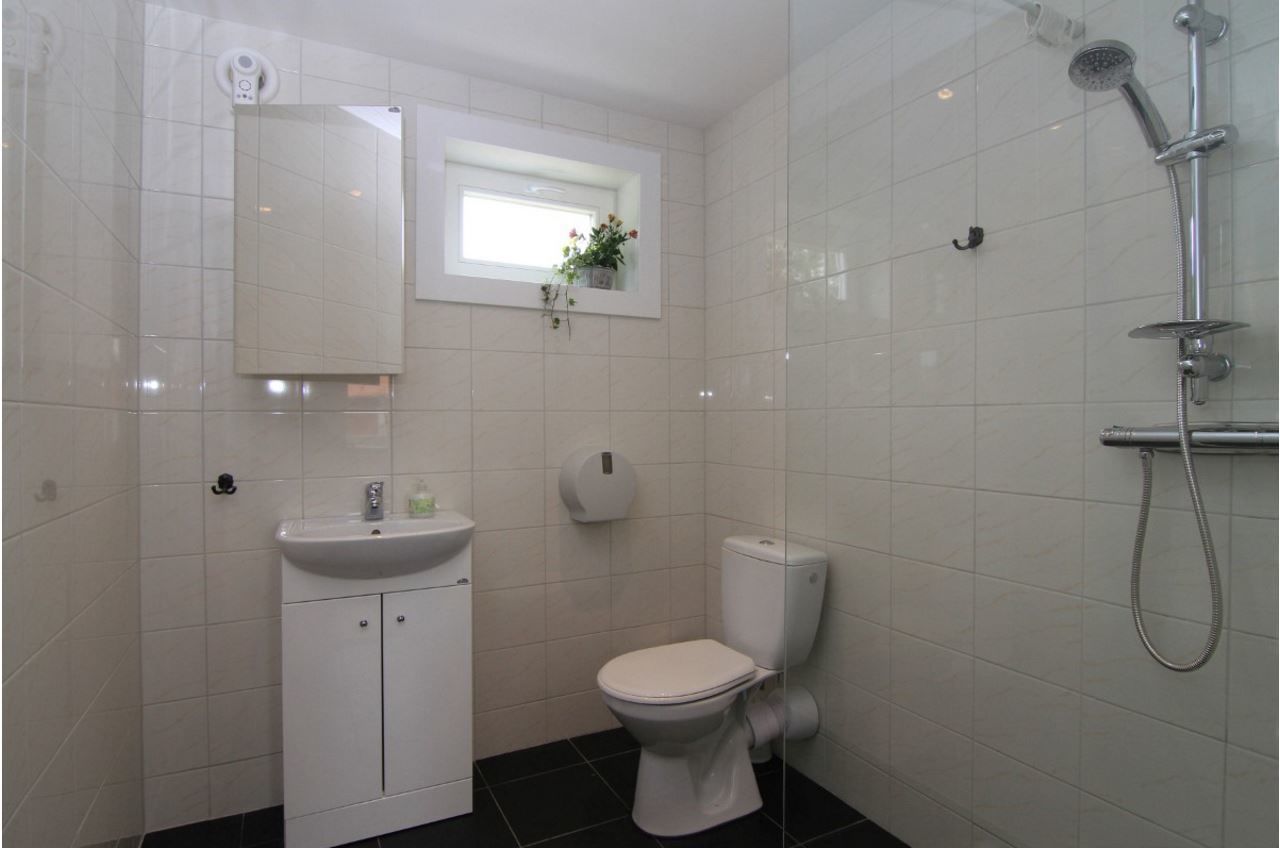Un baño pequeño y limpio con lavamanos, inodoro y ducha blancos.