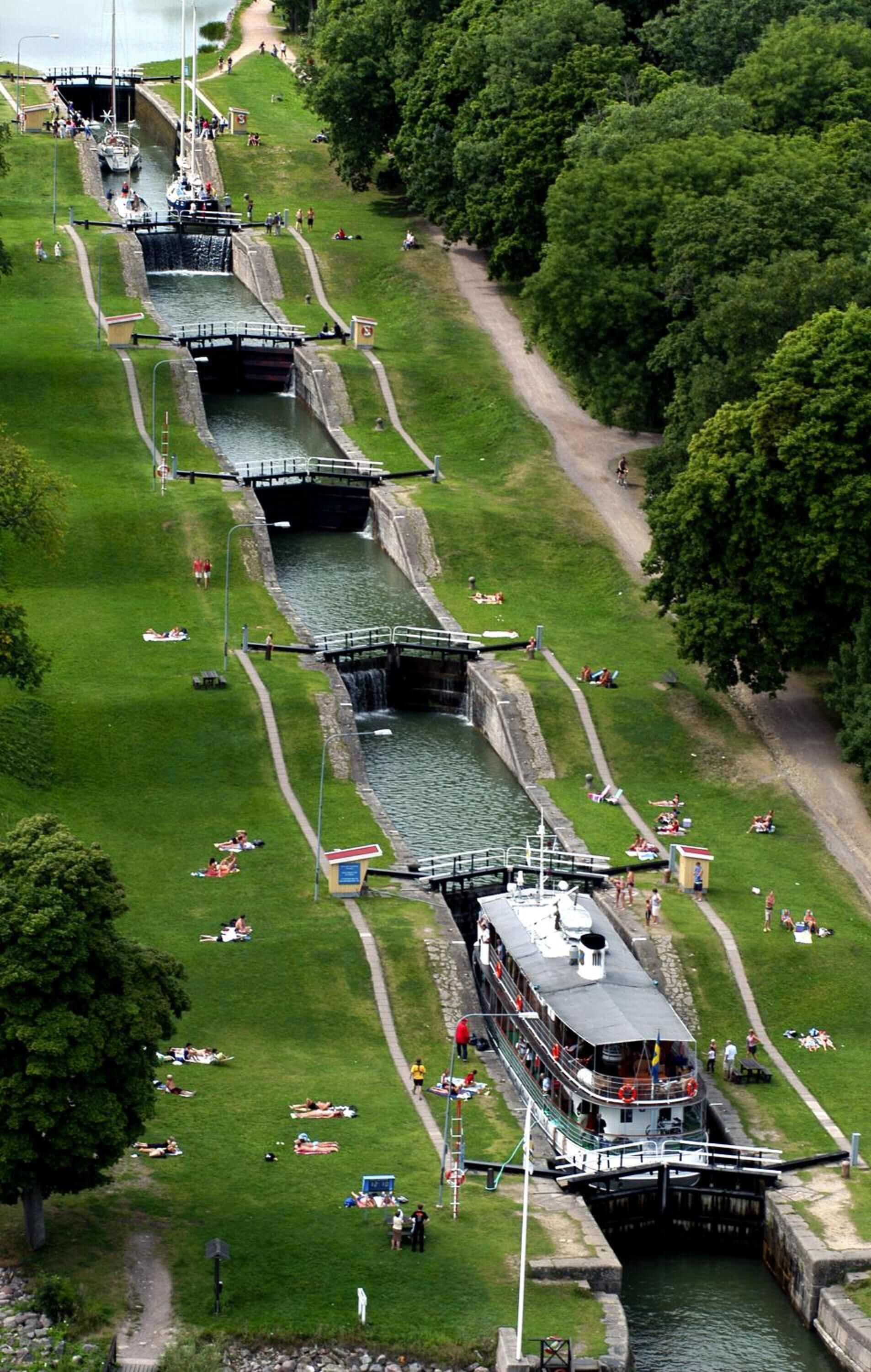 A canal with a boat passing through locks, surrounded by grassy areas and trees.