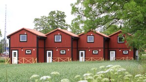 A row of red barns with white doors and windows, surrounded by a grassy field. - Bergs Slussar Vandrarhem & Stugor - Hostel (Vreta Kloster)