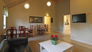 A spacious living area with a high ceiling, a dining table with chairs, a sofa, and a television mounted on the wall. - Bergs Slussar Vandrarhem & Stugor - Hostel (Vreta Kloster)