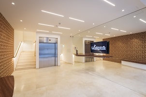 Una hall d'albergo moderna con una reception, una scala e un ascensore.