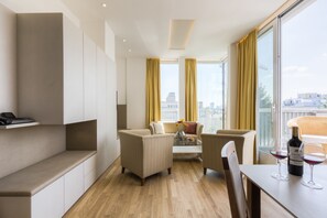 Uma sala de estar moderna com sofá, cadeiras, mesa de centro e mesa de jantar, com copos de vinho e uma garrafa.
