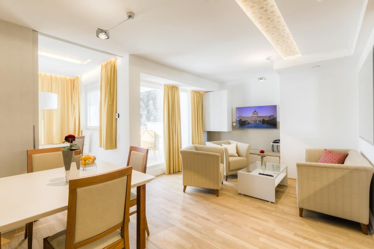 A modern living room with a dining area, featuring a flat-screen TV mounted on the wall, a coffee table, and a sofa.