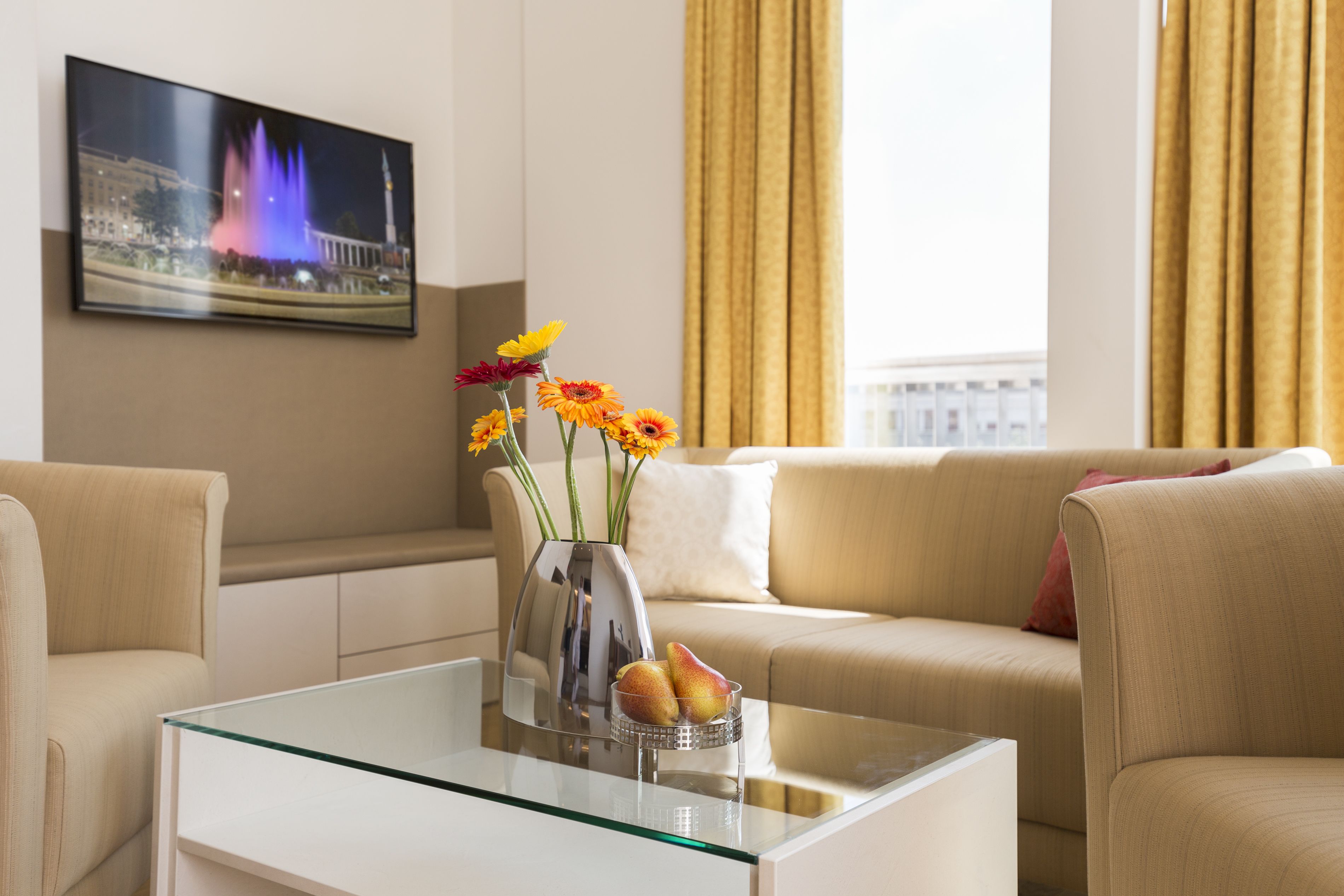 Un salon moderne avec une table basse en verre, un vase de fleurs et un canapé agrémenté de coussins.