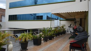 A modern building with a covered outdoor area, potted plants, exercise equipment, and a car parked nearby. - Hotel Las Gardenias (Cuenca)
