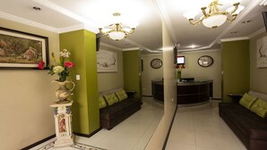 A reception area with a reception desk, two sofas, a vase with flowers, a painting, and a chandelier. - Hotel Las Gardenias (Cuenca)