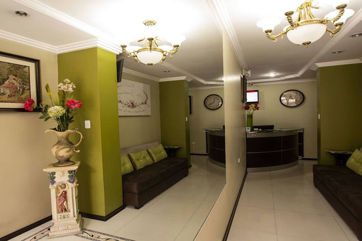 A reception area with a reception desk, two sofas, a vase with flowers, a painting, and a chandelier.
