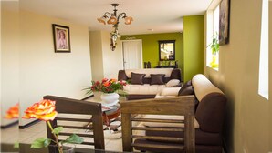 A living room with a sofa, a dining table with chairs, a chandelier, and a vase of flowers. - Hotel Las Gardenias (Cuenca)