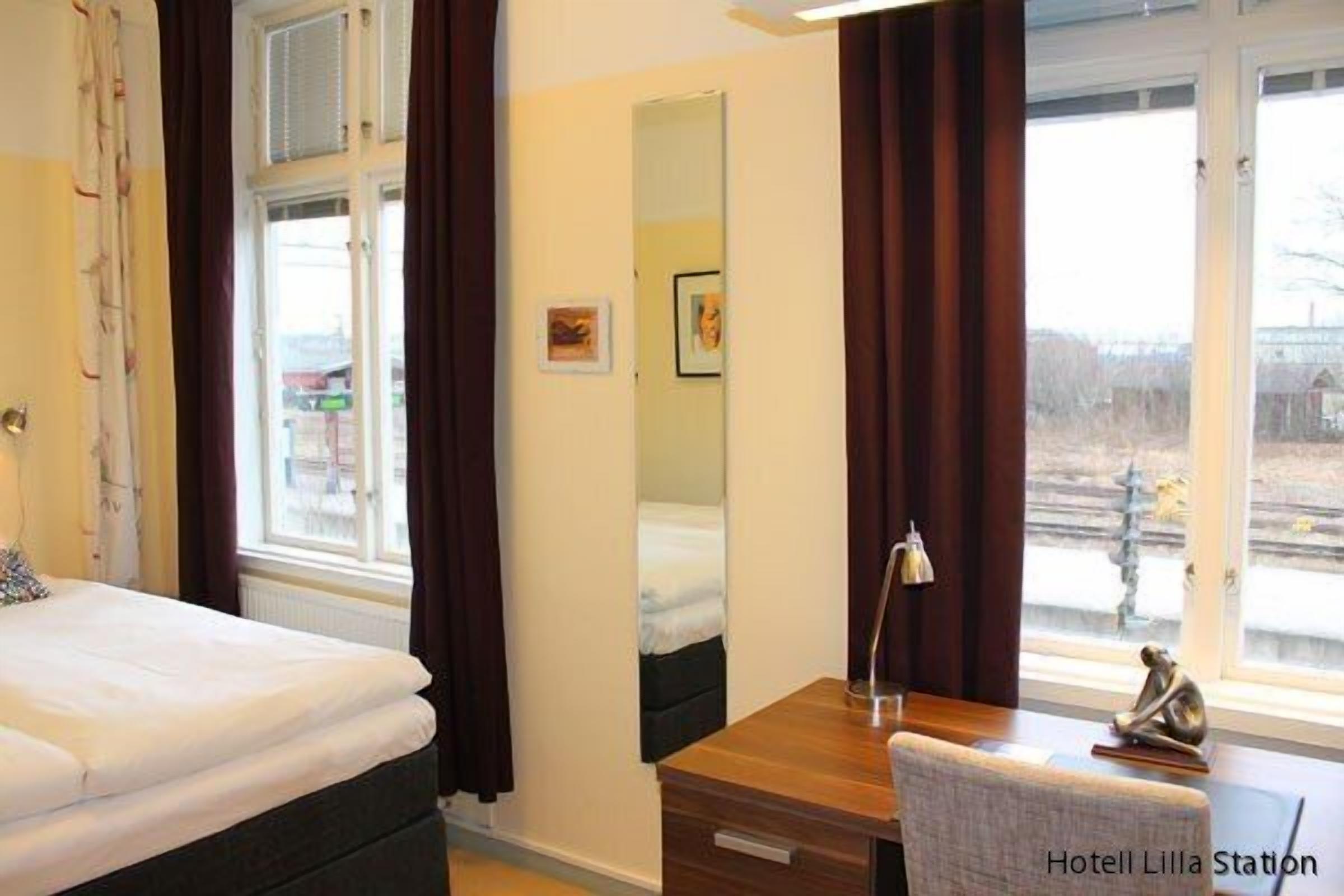 Habitación de hotel con cama, escritorio con silla, espejo y vista al exterior.