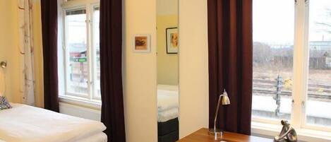 Habitación de hotel con cama, escritorio con silla, espejo y vista al exterior.