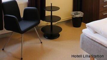 A hotel room with a bed, a TV mounted on the wall, a small round table, a chair, and a window with curtains.