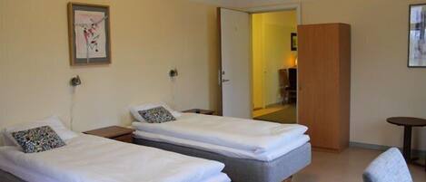 Quarto de hotel com duas camas de solteiro, uma mesa pequena e uma cadeira.