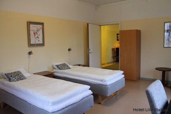 A hotel room with two single beds, a small table, and a chair. - Stationshusets Hotell och Café (Köping)
