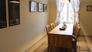 Un coin repas avec une table et des chaises en bois, des tableaux encadrés au mur et une fenêtre avec des rideaux.