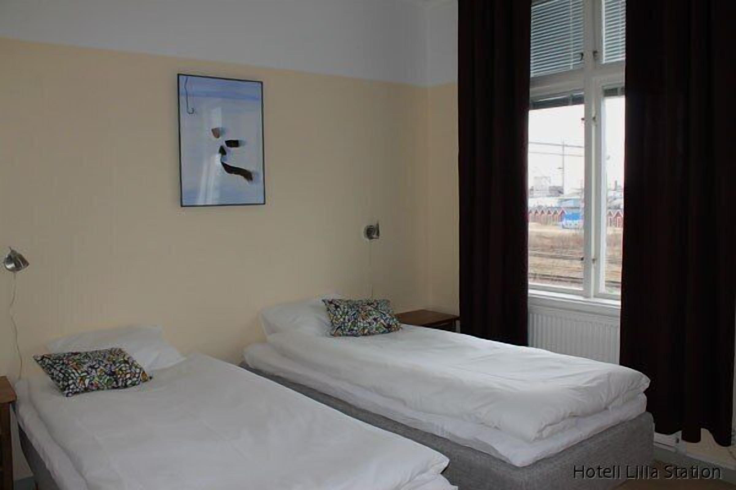A hotel room with two single beds, a window with curtains, a wall-mounted picture, and a view of the outside.