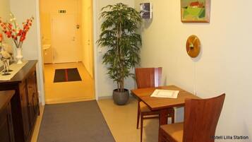 A hotel room with a wooden dining table, chairs, a potted plant, a painting, and a clock on the wall.