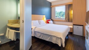 Een hotelkamer met een bed, een klein bureau, een raam met uitzicht en een badkamer met wastafel en toilet.