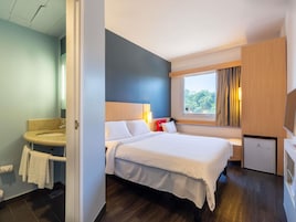 Una habitación de hotel con cama, un escritorio pequeño, una ventana con vistas y un baño con lavabo e inodoro.