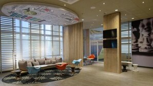 Een moderne hotellobby met een gebogen plafond, een bank, stoelen en een groot raam met jaloezieën.
