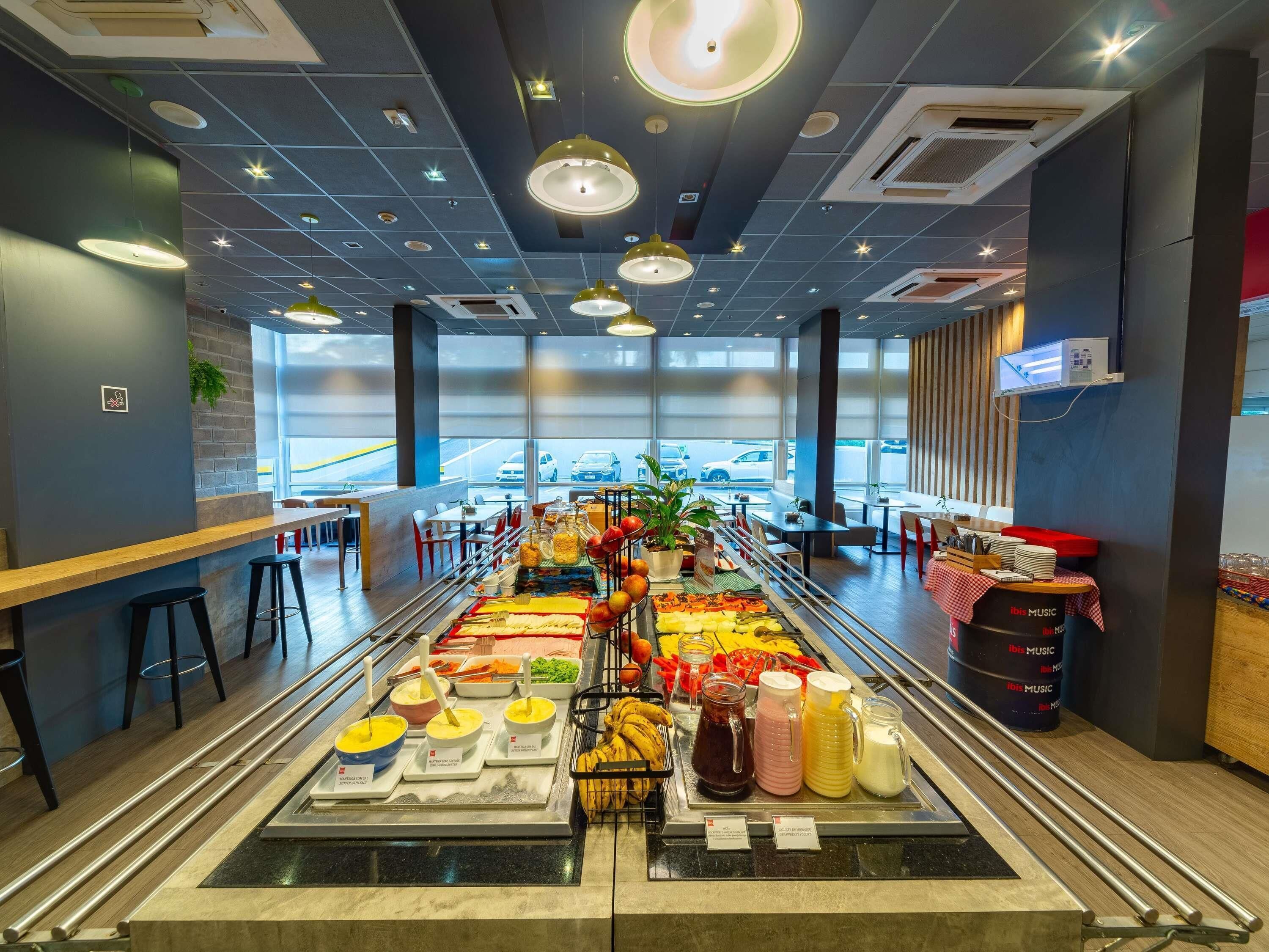 A buffet setup with various food items and drinks, a seating area with tables and chairs, and a modern ceiling design with recessed lighting.