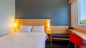 A hotel room with a bed, bedside lamps, a desk with a chair, and a window.