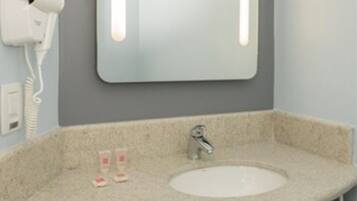 Un baño con un lavabo redondo, un espejo con iluminación, un secador de pelo y toallas.