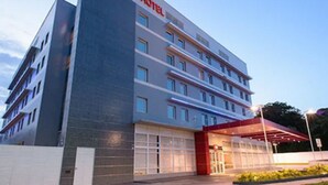 Een modern hotelgebouw met een opvallend “ibis Hotel” bord, verschillende verdiepingen en een overdekte ingang.