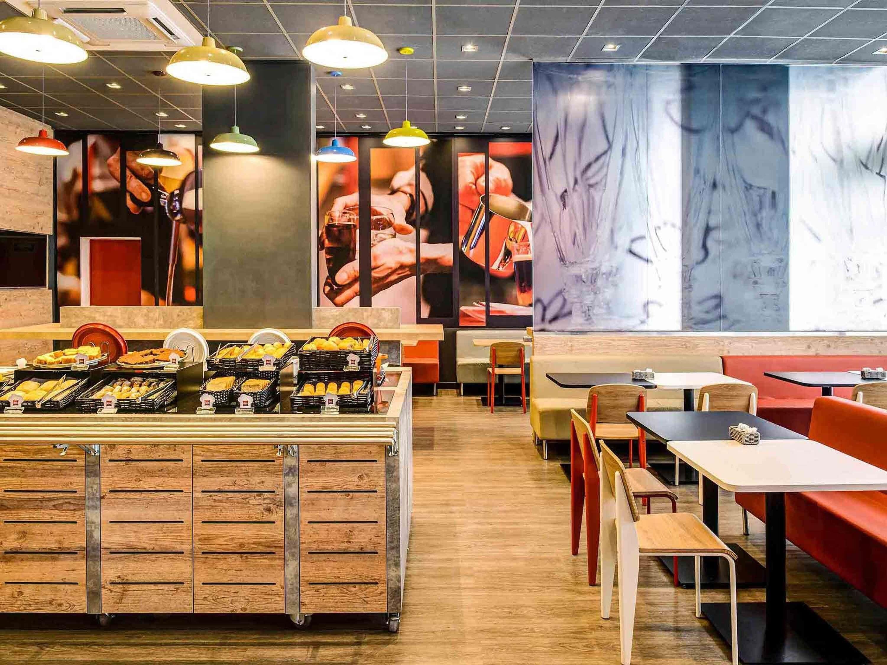 A modern cafe with a wooden counter displaying pastries and a seating area with tables and chairs.
