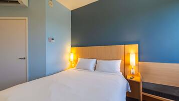 Habitación de hotel con cama, lámparas de noche, mesita de noche, aire acondicionado instalado en la pared y una puerta.