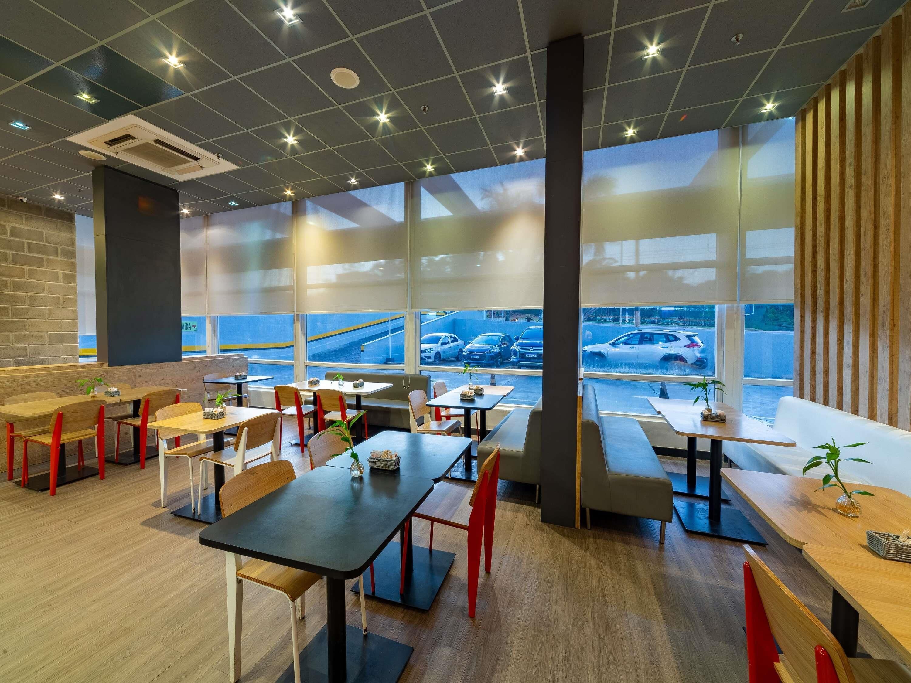 Een modern restaurant met hoge plafonds, grote ramen en uitzicht op een parkeerplaats.