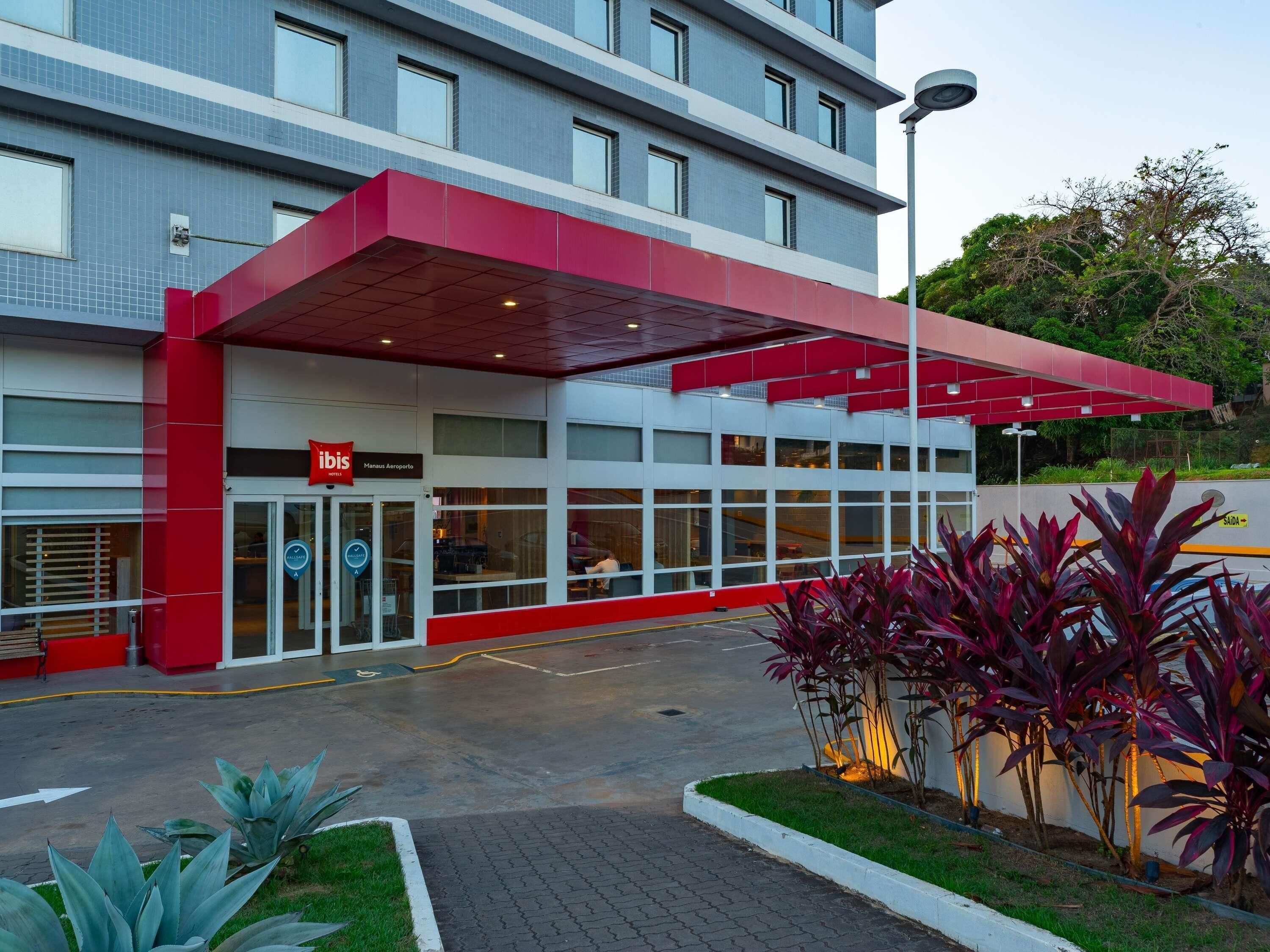 Un edificio moderno con fachada roja y blanca, un acceso cubierto y el letrero del hotel 'ibis'.