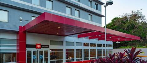 A modern building with a red and white facade, a covered entrance, and a sign for 'ibis' hotel.