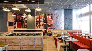 En restaurantindretning med en central ø, borde med siddepladser og hængende lamper.
