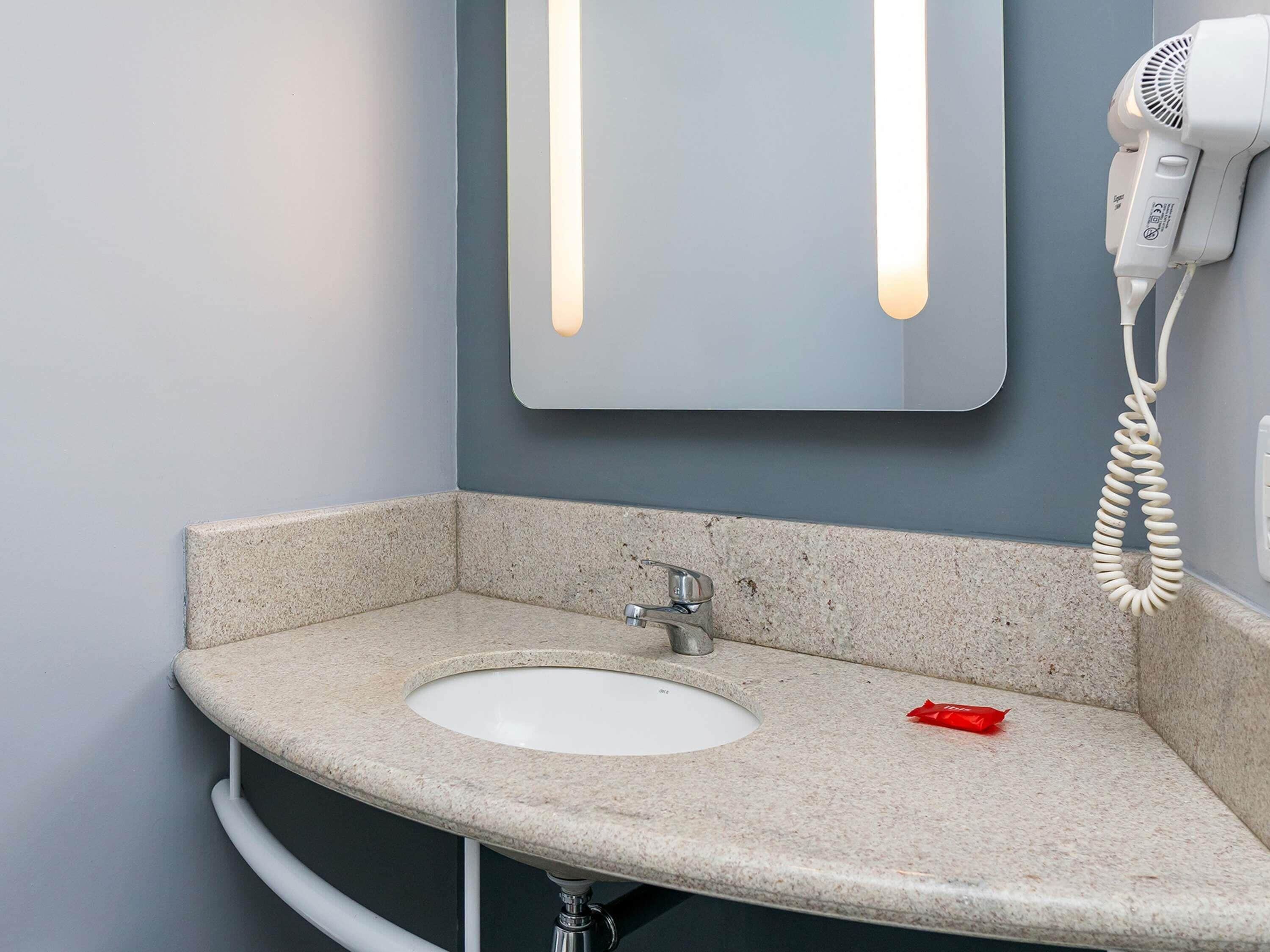 Une salle de bain équipée d’un lavabo, d’un miroir et d’un sèche-cheveux.