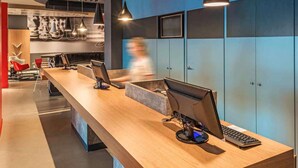 A modern reception desk with multiple computer stations, a long counter, and a person walking by. - ibis Chapeco (Chapecó)