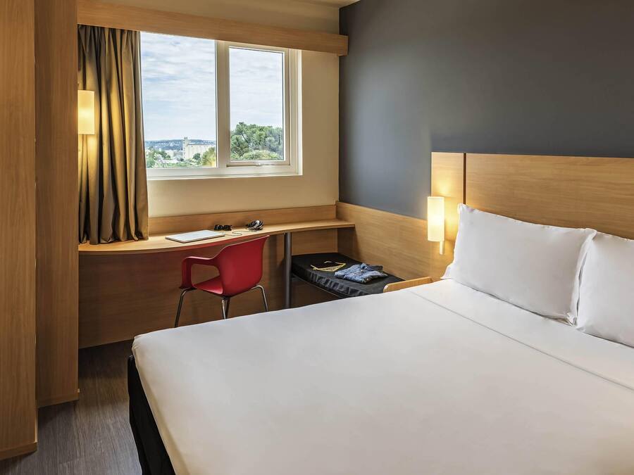 A hotel room with a bed, a desk, a chair, and a window with curtains.