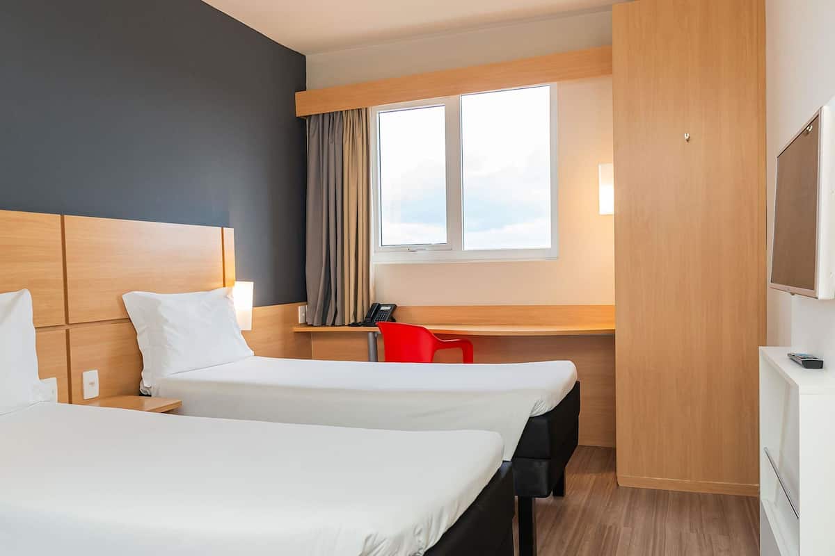 Habitación de hotel con dos camas, un escritorio, una silla, un televisor y una ventana con cortinas.