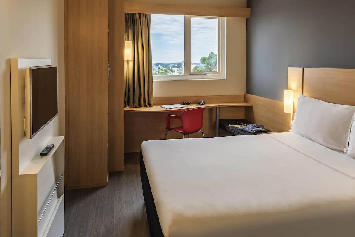 Habitación de hotel con cama, escritorio, silla, televisor y ventana con vistas.