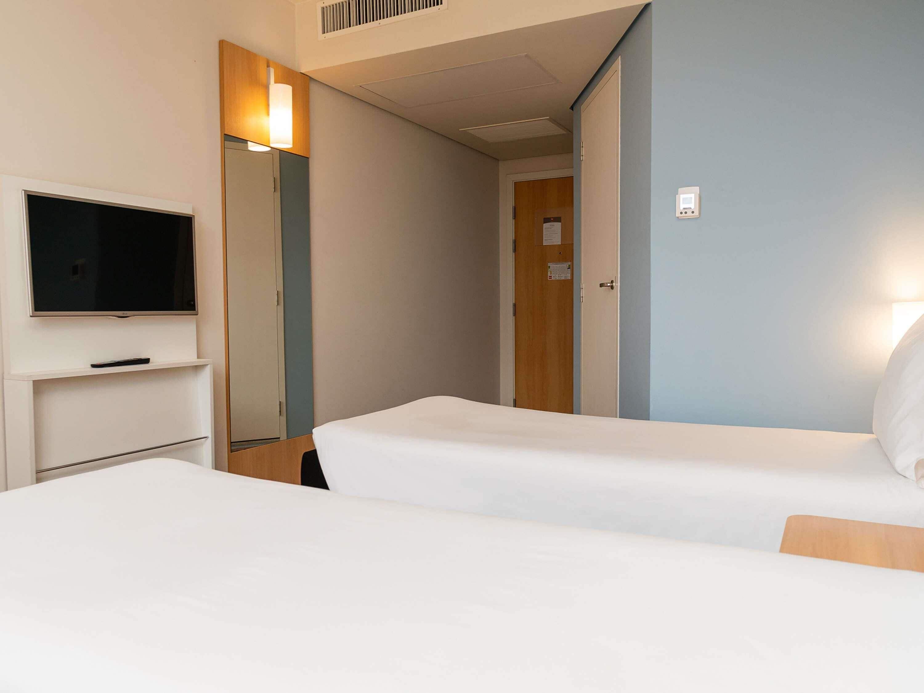 Ett hotellrum med två sängar, en TV, en spegel och en dörr.