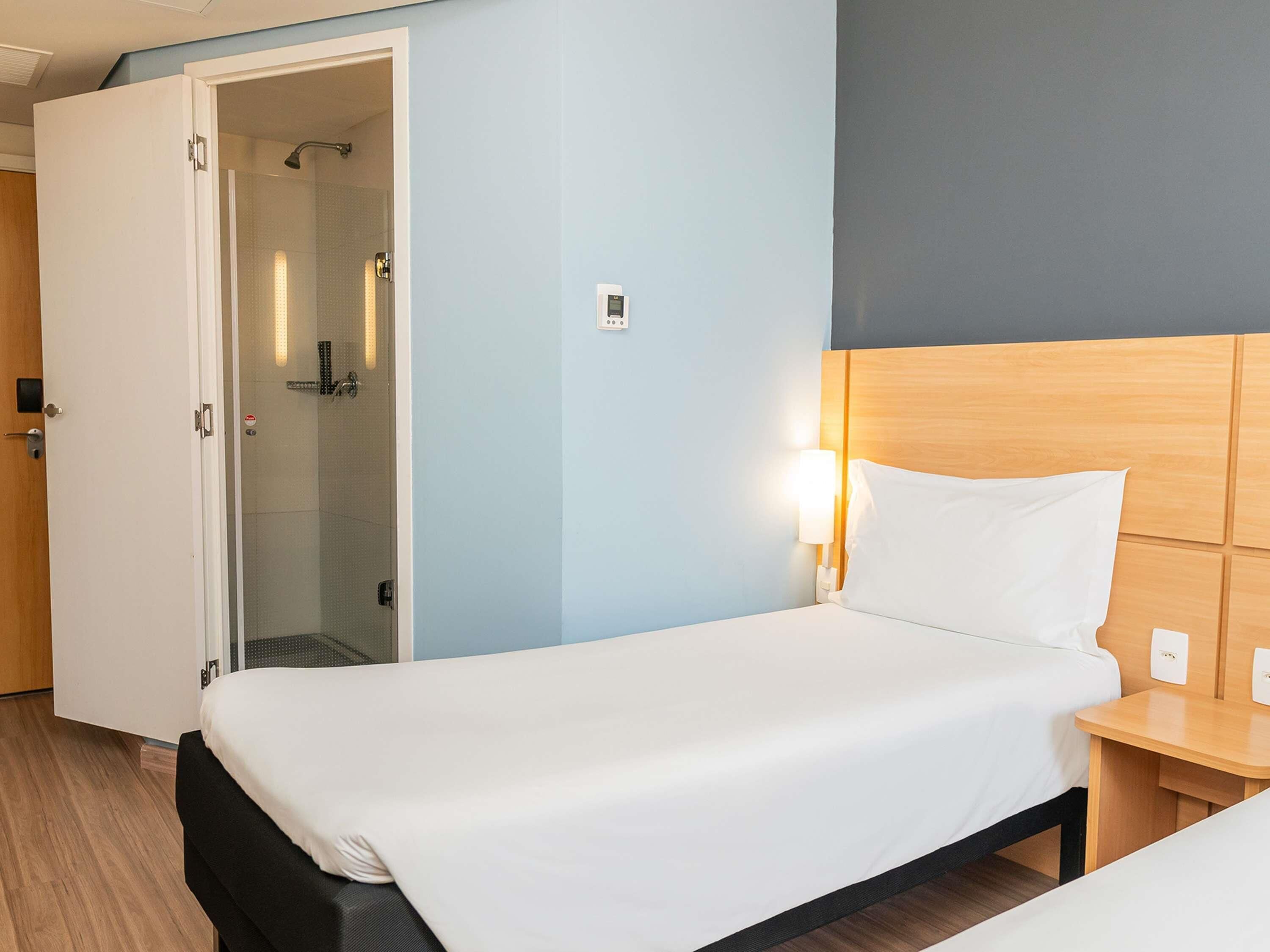 Habitación de hotel con cama, mesita de noche y zona de ducha.