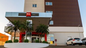 A modern hotel with a prominent 'ibis' sign, a covered entrance, and a parking area with cars. - ibis Chapeco (Chapecó)
