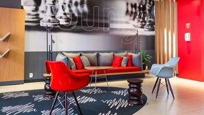 A modern lounge area with a sofa, red and blue chairs, a wooden table, and a black and white patterned rug. - ibis Chapeco (Chapecó)