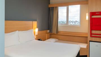Quarto de hotel com cama grande, escrivaninha, cadeira, mini-frigorífico, janela com cortinas e vista para a cidade.